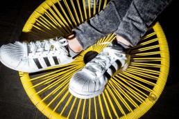 Close up flash street photograph of a pair of feet wearing Adidas shoes on top of a yellow chair