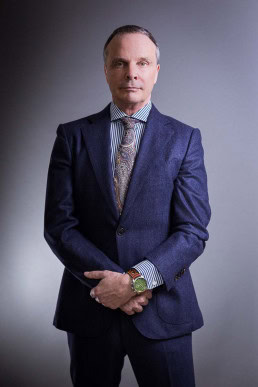 Corporate portrait of a man in suit and tie against a dark background
