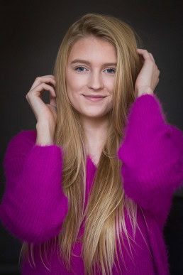 Headshot portrait of a blond woman wearing a fuchsia sweater against a dark background