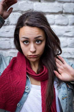 Portrait of a dark-haired woman wearing a jean jacket and a red scarf against a white brick wall