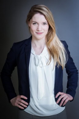 Corporate portrait of a young blond-hair woman wearing a jacket against a dark background