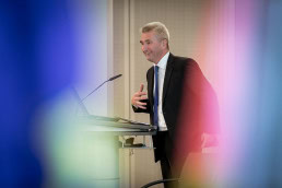 A speaker smiles while giving a presentation during a conference meeting in Brussels