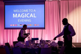 A screen announces 'Welcome to a Magical Evening' during an event in Brussels