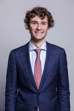 Corporate portrait of a young man wearing a blue suit with a pink tie