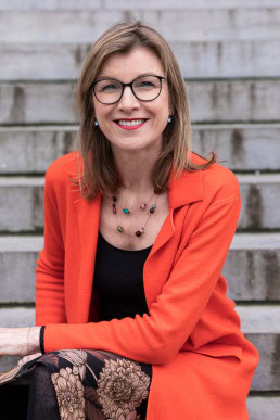 Portrait of Birgitta Bechtold wearing a red jacket while smiling to the camera