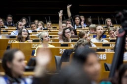 A woman in the audience raises her hand at the EU Parliament