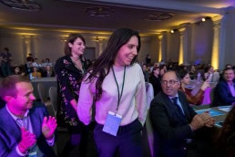 A woman wins a prize and approaches the podium while smiling in excitement at the EUSIC 2019 awards