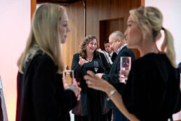 A woman smiling while networking in the background and two women also networking with drinks in the foreground