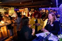 A room full of people networking and three women in the foreground speaking during the NYC Tourism Convention in Brussels