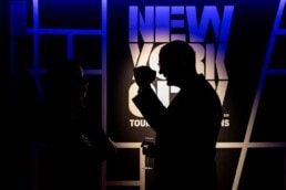 The silhouette of a man making a hand gesture in front of the New York City Tourism's logo during the NYC Tourism Convention in Brussels