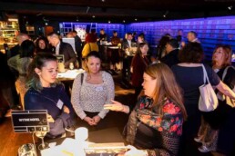 A room full of people talking and engaging in conversation while three women are on the foreground during the NYC Tourism Convention in Brussels