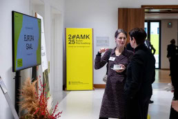 Two people speaking during a lunch break at a conference in Brussels. Banners of the conference can be seen in the background