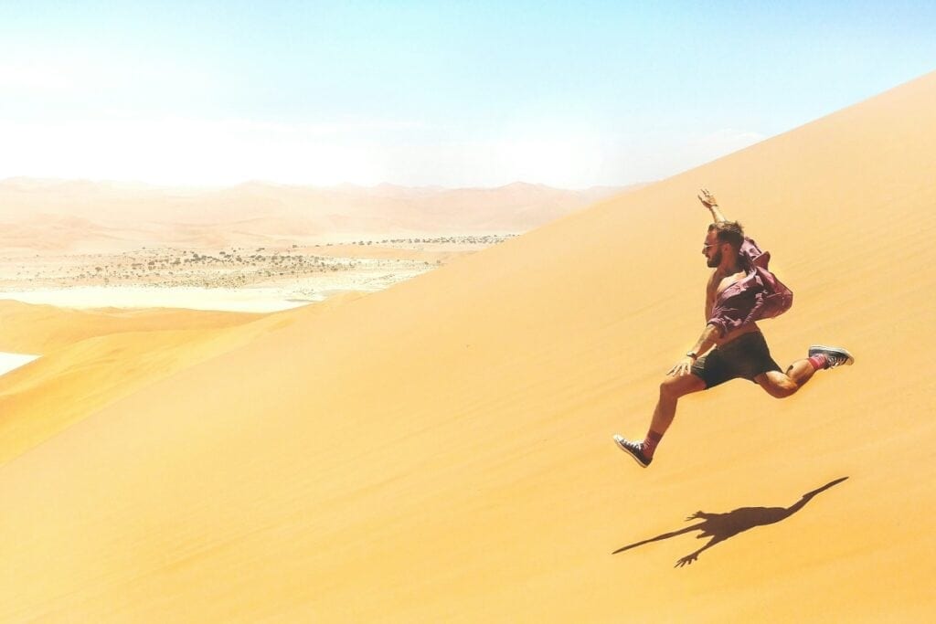 A man runs down a sand dune.