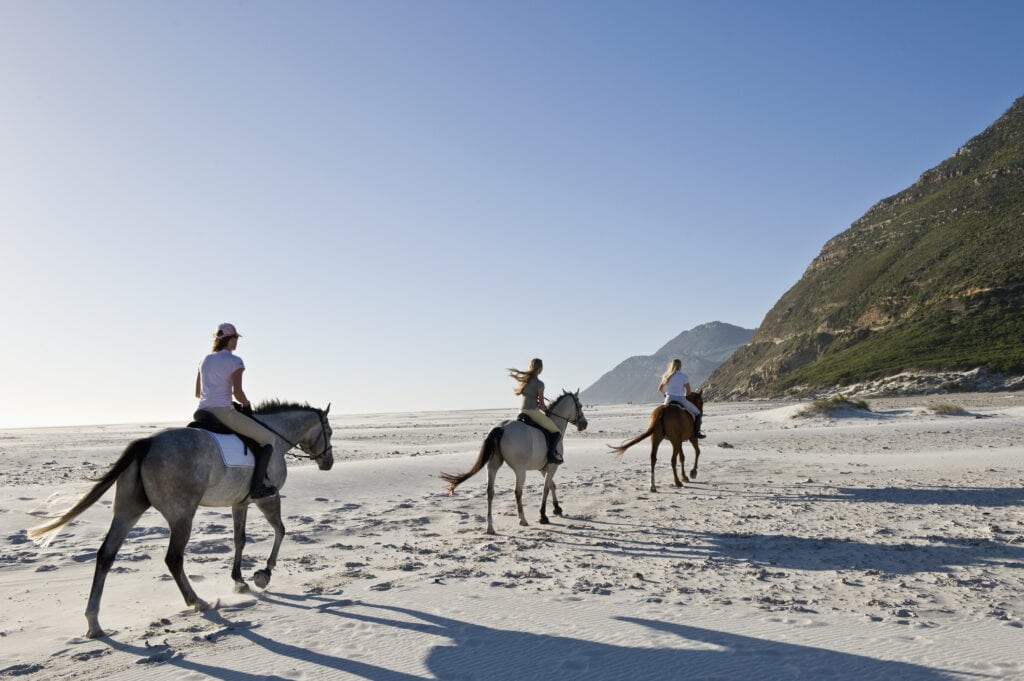 Three people riding horses on a beach in South Africa. Photo: Getty Images