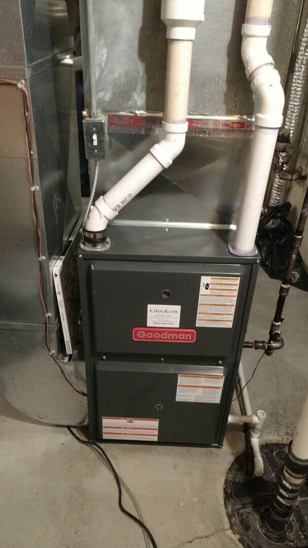 HVAC furnace with white PVC pipes in a utility room.