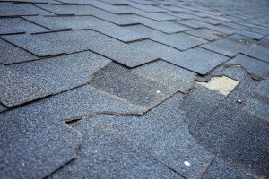 Damaged asphalt shingles on a roof with missing and cracked shingles.