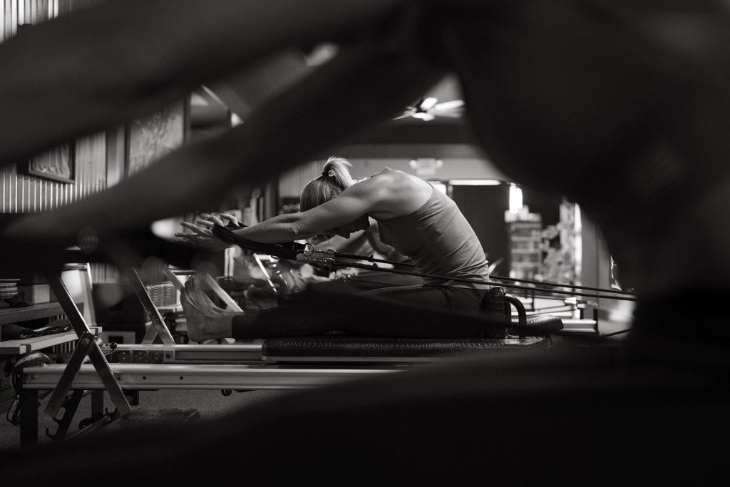 Woman stretching on reformer machine during Pilates class at Grit Pilates and Yoga.