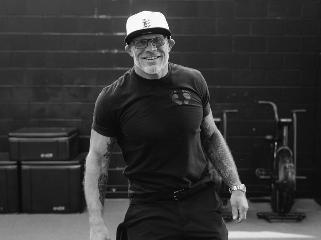 Smiling male instructor in black T-shirt and cap at Grit Pilates and Yoga.