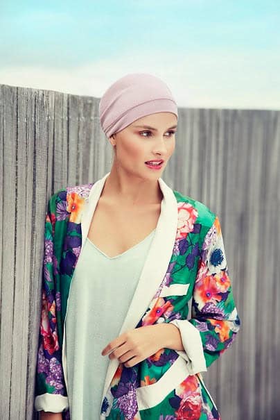 Woman wearing a pink turban and colorful floral blazer outdoors.