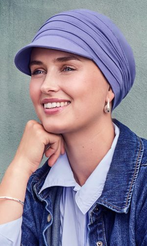 Woman with a purple headwrap, denim jacket, and white shirt smiling outdoors.