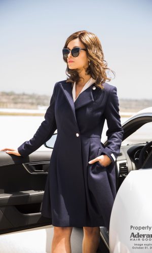 Stylish woman with wavy hair wearing sunglasses and a navy coat outdoors.