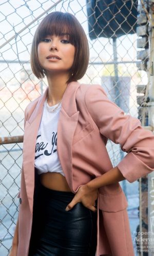 Woman with short bob wig, stylish pink blazer, urban background.