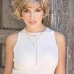 Stylish short blonde wavy wig on a woman with a rustic background.