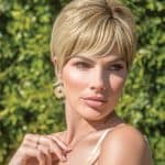 Short blonde bob wig on a woman outdoors with green foliage background.
