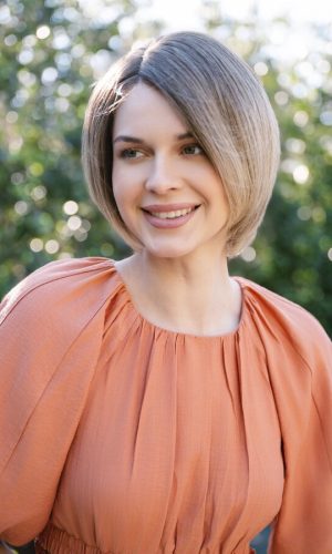 Woman with short, layered bob wig outdoors, smiling, natural sunlight.