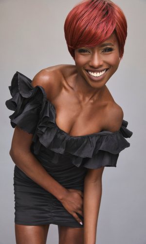 Woman with vibrant red short wig and black ruffled dress smiling.