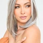Woman with long silver wavy wig, natural makeup, and soft expression.