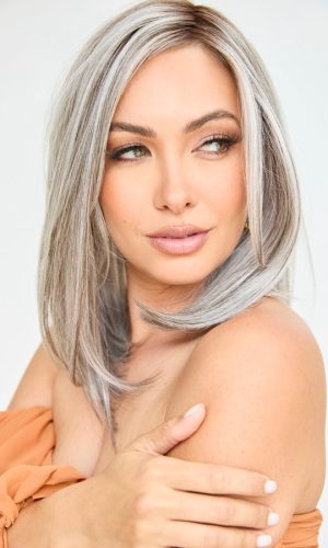 Woman with long silver wavy wig, natural makeup, and soft expression.