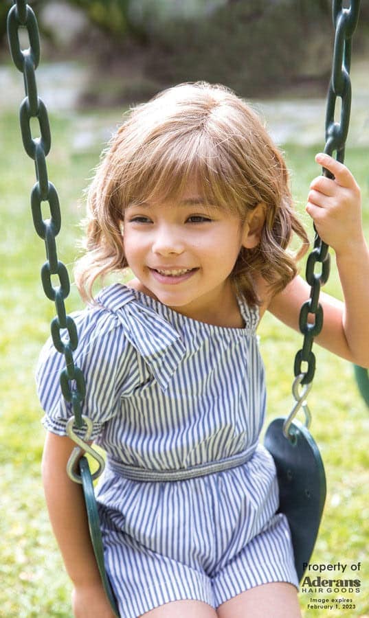 Young girl with wavy blonde wig smiling on a swing in a park.
