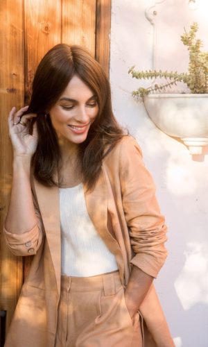Woman with long brown wig smiling outdoors in natural light.