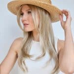 Woman wearing a wide-brimmed straw hat and blonde wig, looking to the side.