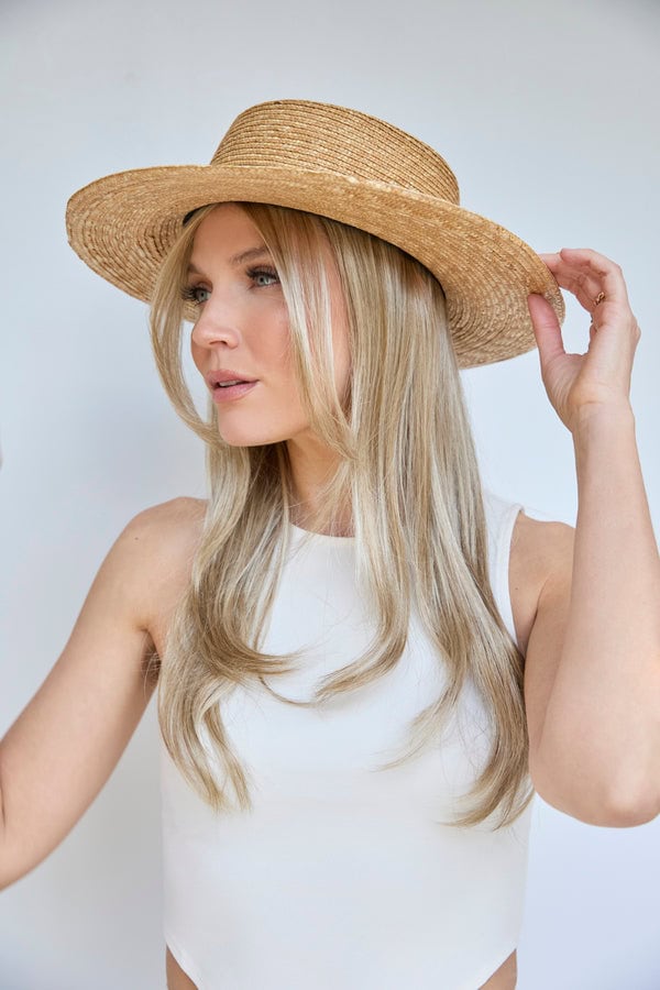 Woman wearing a wide-brimmed straw hat and blonde wig, looking to the side.