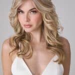 Beautiful blonde wavy wig on a woman with natural makeup and a white dress.