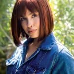 Woman wearing a straight red bob wig outdoors in natural light.