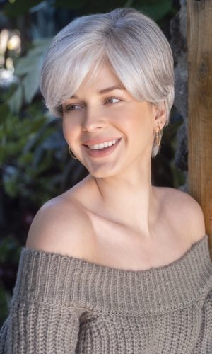 Woman with short, silver wig smiling outdoors in natural light.