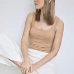 Woman with blonde hair wearing a beige cap, beige tank top, and white pants.