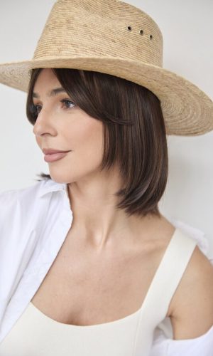 Woman with short brown hair wearing a large straw hat and white top.