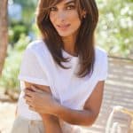 Woman with layered brown wig outdoors, natural sunlight, smiling, casual white top.