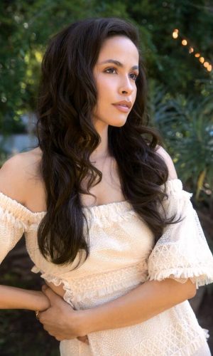 Woman with long, wavy dark brown wig outdoors, natural makeup, stylish look.