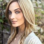 Blonde woman with wavy hair and natural makeup outdoors.