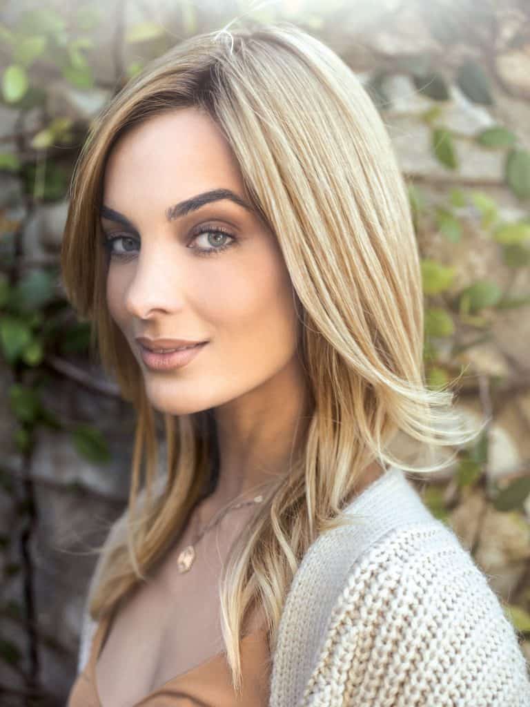 Blonde woman with wavy hair and natural makeup outdoors.