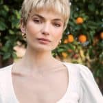 Woman with short blonde wig outdoors, natural makeup, and white blouse.
