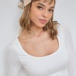 Woman wearing a beige bandana with black logo and a white top.