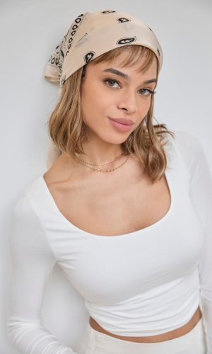 Woman wearing a beige bandana with black logo and a white top.