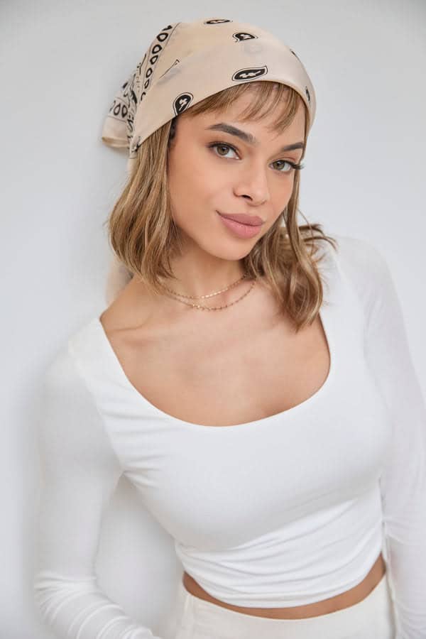 Woman wearing a beige bandana with black logo and a white top.