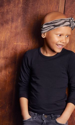 Young girl with headband smiling against wooden background.